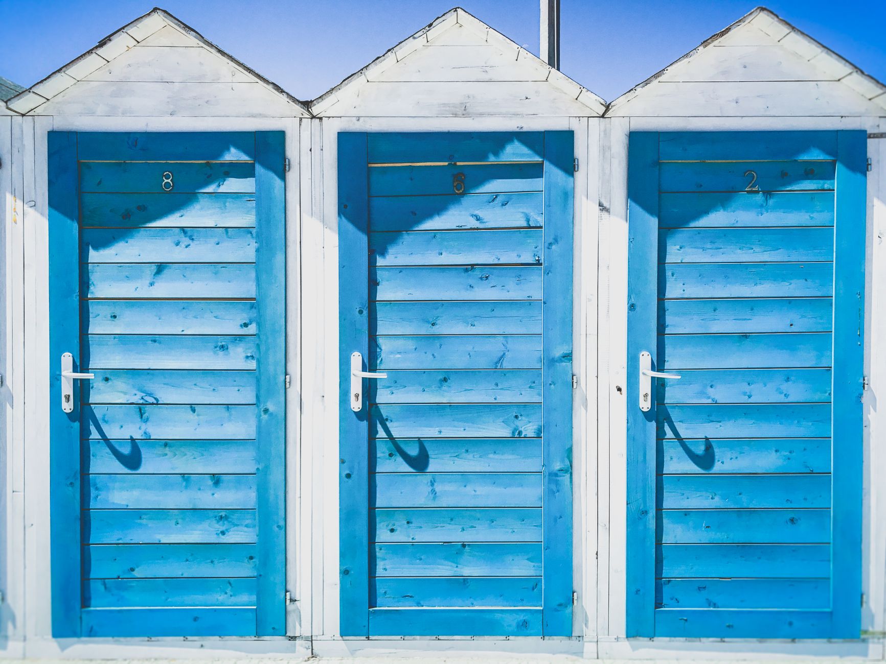 Three vibrant blue beach huts under a clear sky